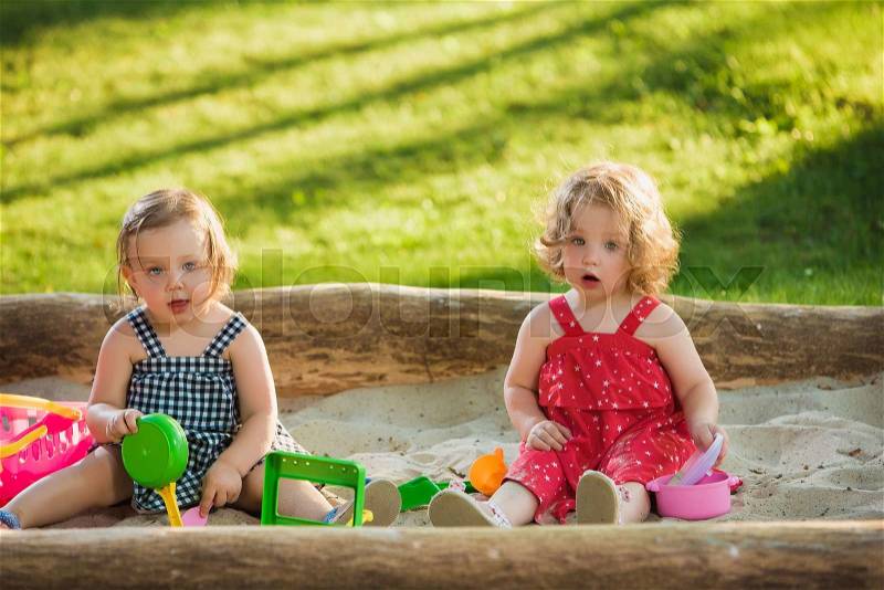 The two little baby girls two-year old playing toys in sand against green grass, stock photo