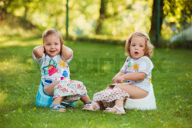 The two little baby girls two-year old sitting on pots against green grass, stock photo
