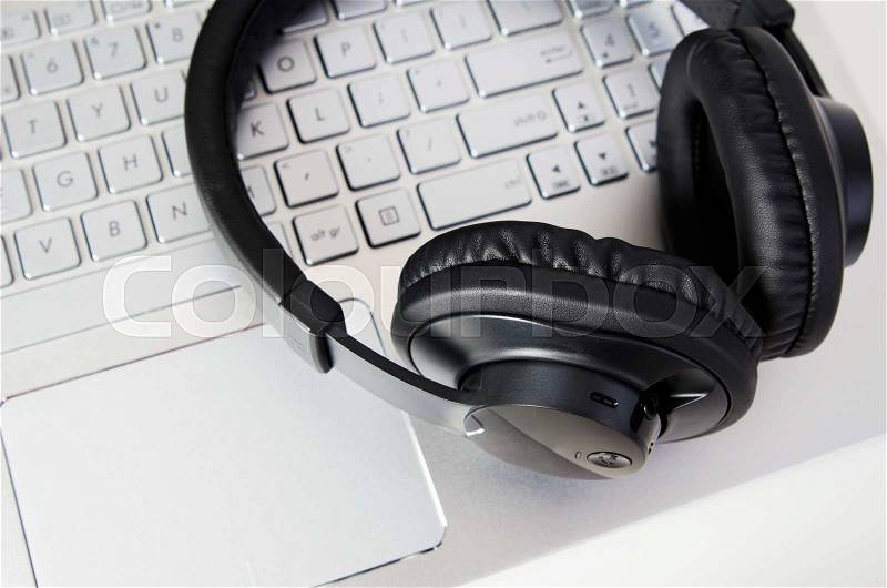Wireless headphones on laptop keyboard. Music and gaming devices concept, stock photo