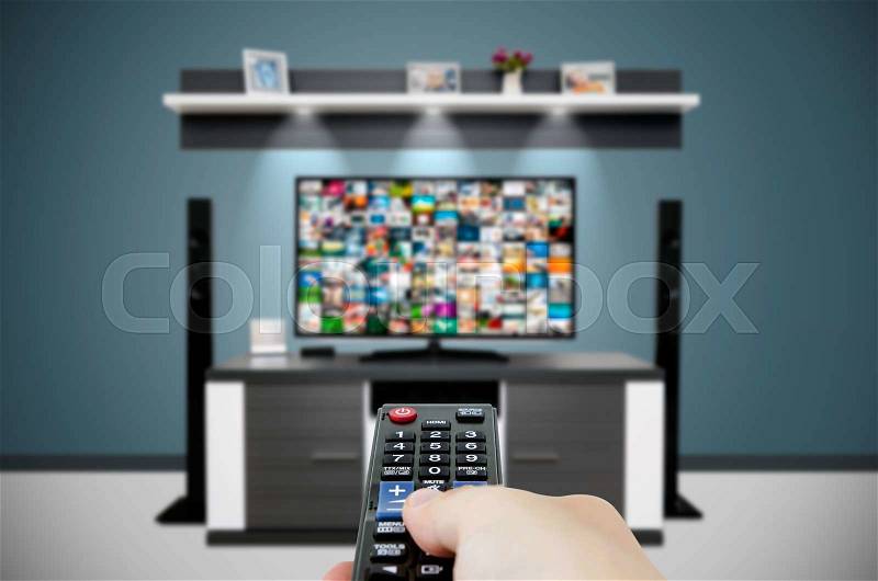 Watching television in modern TV room. Hand holding remote control, stock photo
