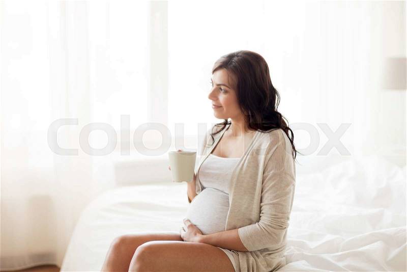 Pregnancy, drinks, rest, people and expectation concept - happy pregnant woman with cup drinking tea sitting on bed at home bedroom, stock photo