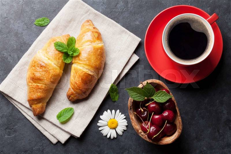 Fresh croissants, cherry berries and coffee cup on stone table. Top view. Breakfast concept, stock photo