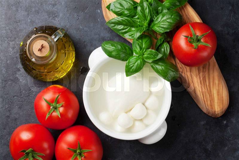 Mozzarella cheese, tomatoes and basil herb leaves over stone table. Top view, stock photo