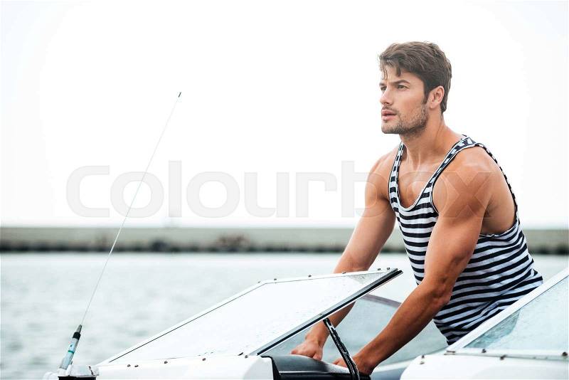 Young handsome bearded sailor man driving his motor boat, stock photo