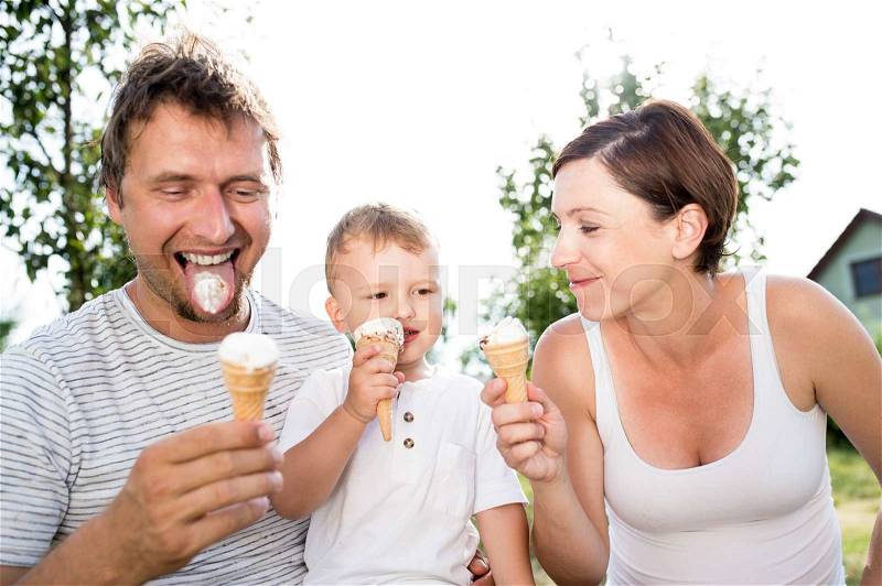 Young parents with their little son eating ice cream, sunny summer garden, stock photo