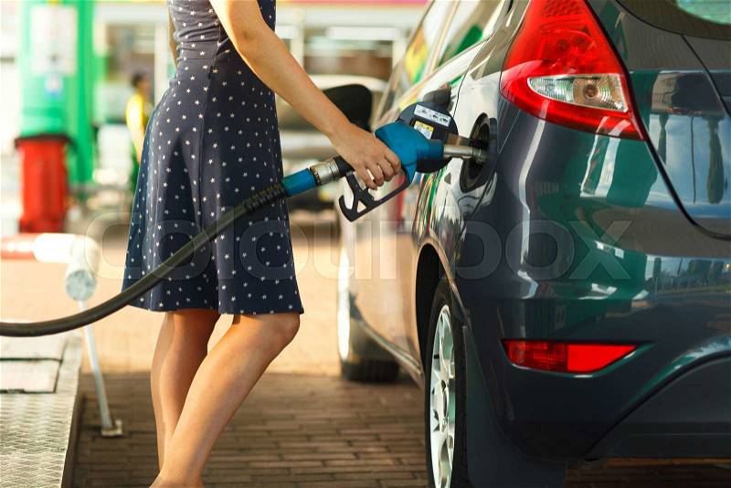 Woman fills petrol into her car at a gas station, stock photo