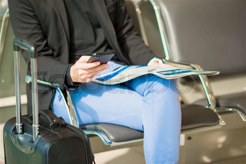 Young caucasian man with newspaper and cellphone at the airport while waiting for boarding. Casual young businessman wearing suit jacket, stock photo