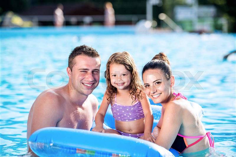 Young mother and father with their daughter sitting on pool lilo in swimming pool in aqua park. Summer heat and water, stock photo
