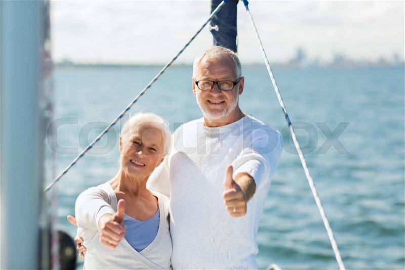 Sailing, age, tourism, travel and people concept - happy senior couple hugging on sail boat or yacht deck floating and showing thumbs up in sea, stock photo