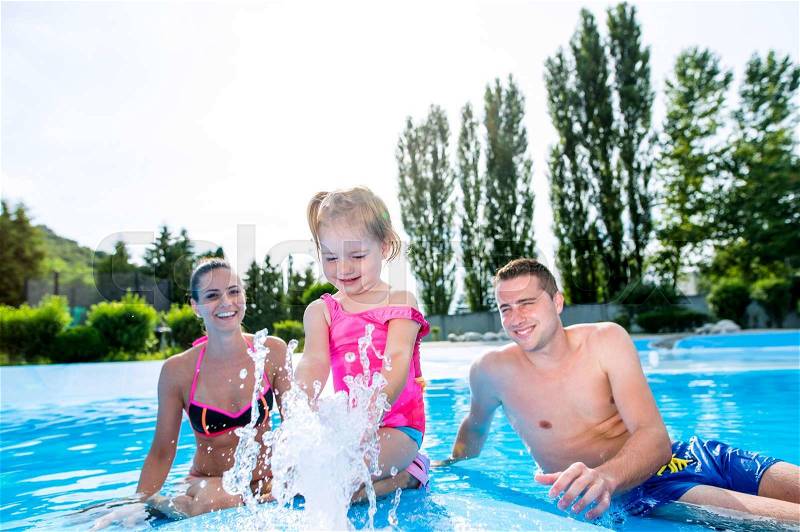 Young mother and father with their daughter in swimming pool in aqua park. Summer heat and water, stock photo