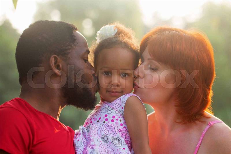 Multiracial mixed family concept. Black father and white mother kissing baby daughter, stock photo
