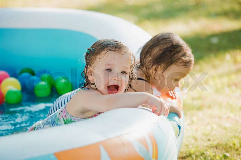 The two Two-year old little baby girls playing with toys in inflatable pool in the summer sunny day, stock photo