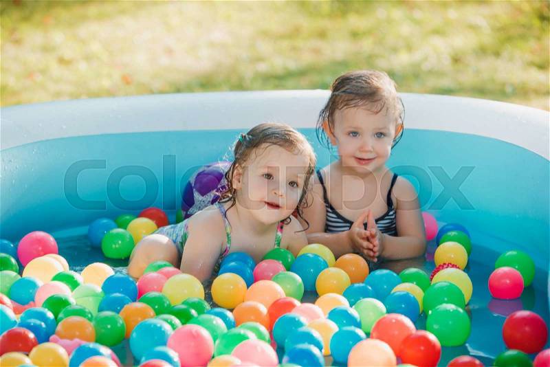 The two Two-year old little baby girls playing with toys in inflatable pool in the summer sunny day, stock photo