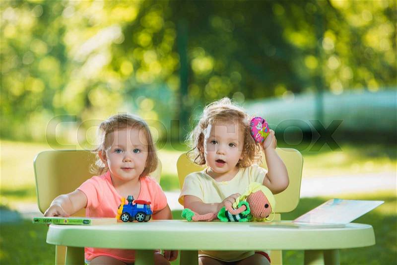 The two little baby girls two-year old playing toys in sand against green grass, stock photo