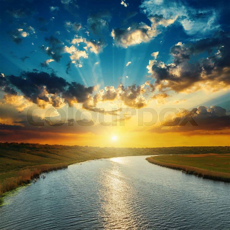 Sunset with clouds, light rays over river with reflections, stock photo