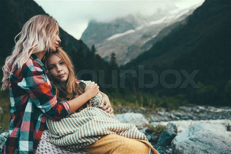 Mom with daughter wrapped in warm blanket outdoor, hiking in mountains, bad cold weather with fog, stock photo