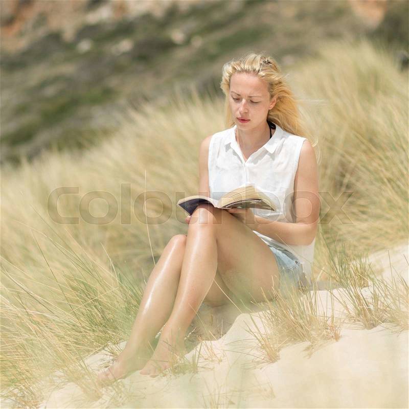 Relaxed woman enjoying sun, freedom and good book an beautiful sandy beach of Balos in Greece. Young lady reading, feeling free and relaxed. Vacations, freedom, happiness, enjoyment and well being, stock photo