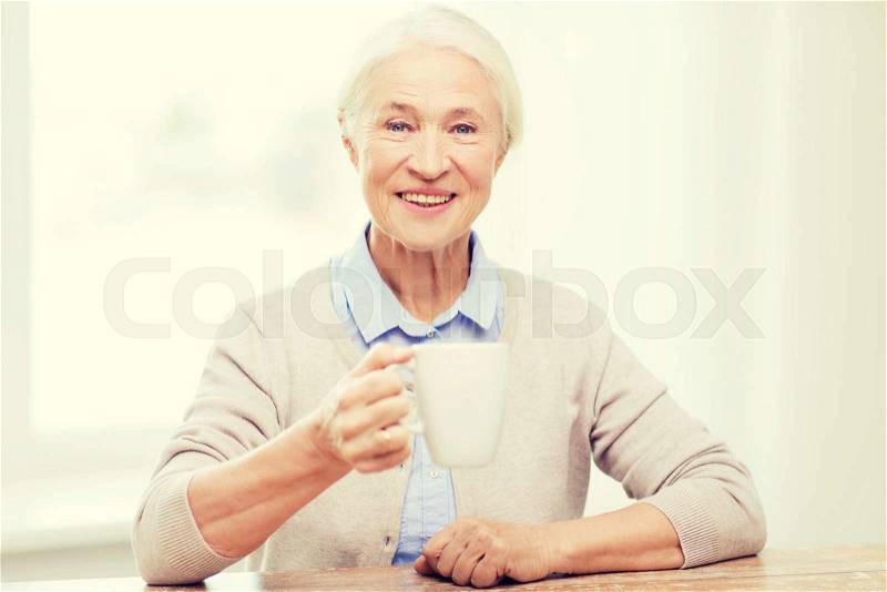 Age, drink and people concept - happy smiling senior woman with cup of tea or coffee at home, stock photo