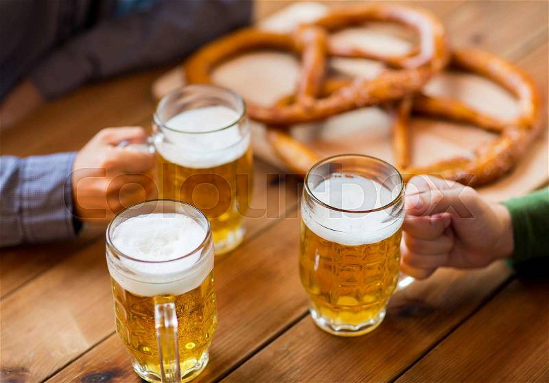 People, leisure and drinks concept - close up of male hands with beer mugs and pretzels at bar or pub, stock photo