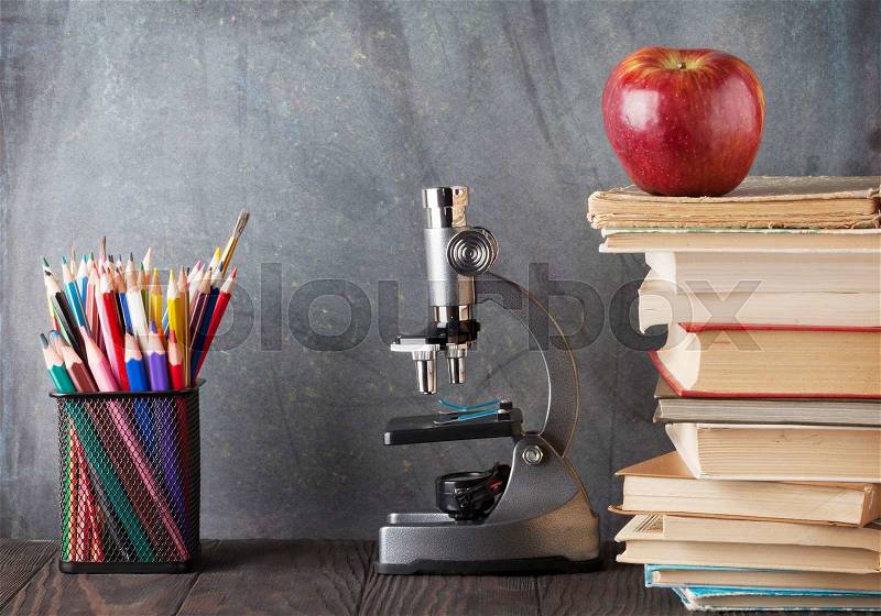Microscope, pencils, books and apple in front of classroom chalk board. Back to school concept with copy space, stock photo