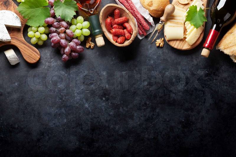 Red and white wine bottles, grape, cheese and sausages over stone table. Top view with copy space, stock photo