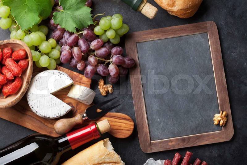 Red and white wine, grape, cheese and sausages over stone table. Top view with blackboard for copy space, stock photo