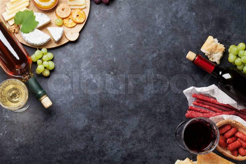 Red and white wine, grape, honey, cheese and sausages over stone table. Top view with copy space, stock photo