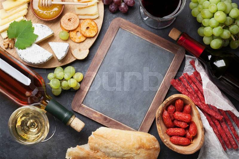 Red and white wine, grape, honey, cheese and sausages over stone table. Top view with blackboard for copy space, stock photo