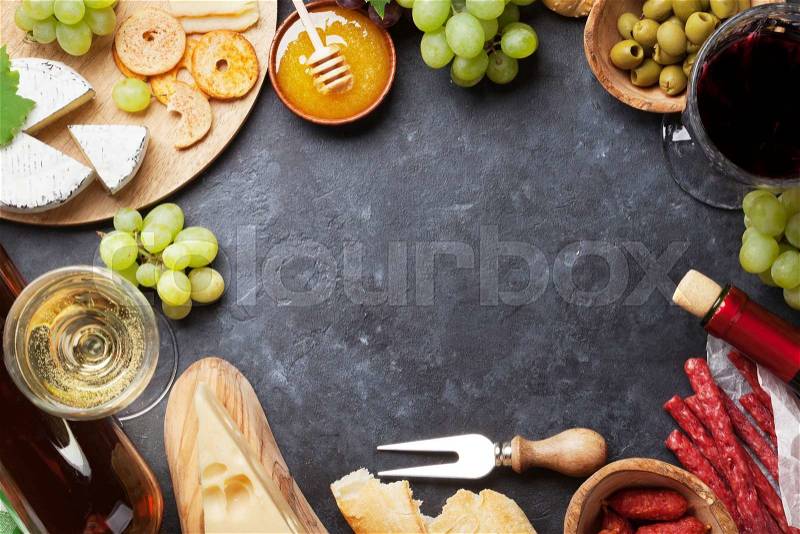 Red and white wine, grape, honey, cheese and sausages over stone table. Top view with copy space, stock photo