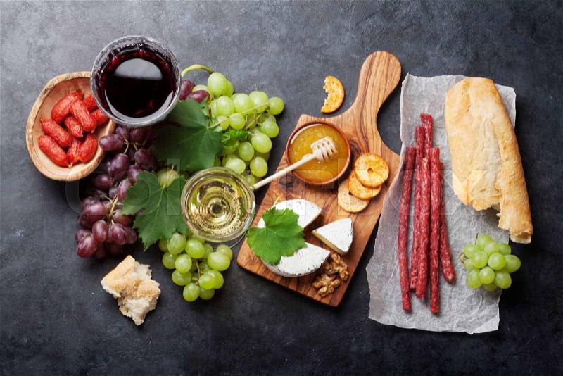 Red and white wine, grape, honey, cheese and sausages over stone table. Top view, stock photo