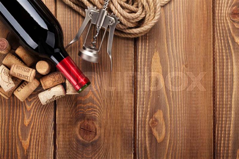 Red wine bottle, corks and corkscrew over wooden table background. Top view with copy space, stock photo