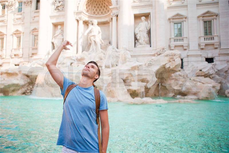 Happy man tourist trowing coins at Trevi Fountain, Rome, Italy for good luck. Caucasian guy making a wish to come back, stock photo