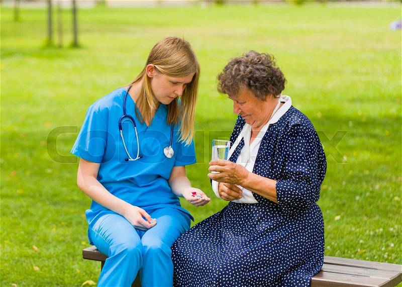 Elder woman patient and doctor sitting on bench holding rehabilitation pills, stock photo