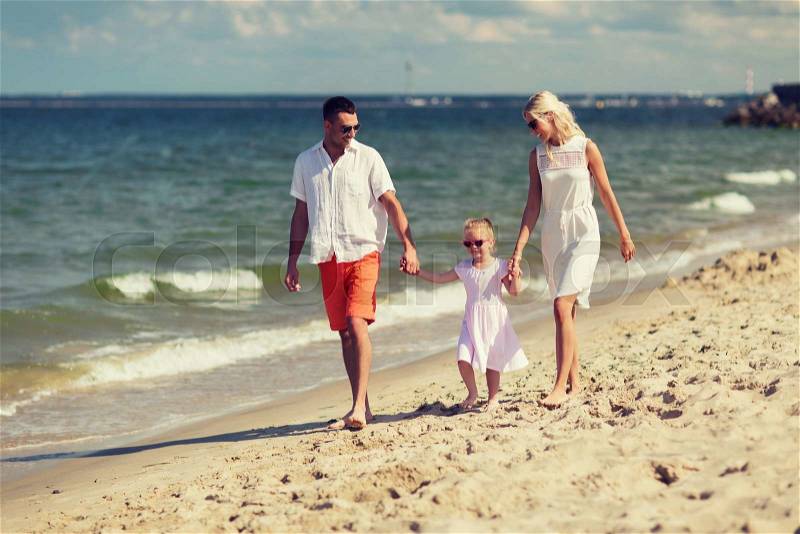Family, vacation, adoption and people concept - happy man, woman and little girl in sunglasses walking on summer beach, stock photo