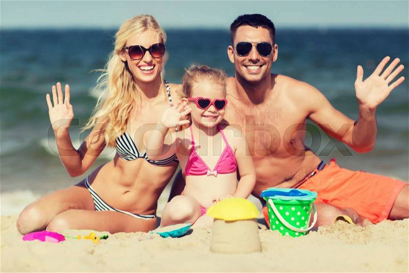 Family, travel, vacation and people concept - happy man, woman and little girl in sunglasses with sand toys waving hands on summer beach, stock photo