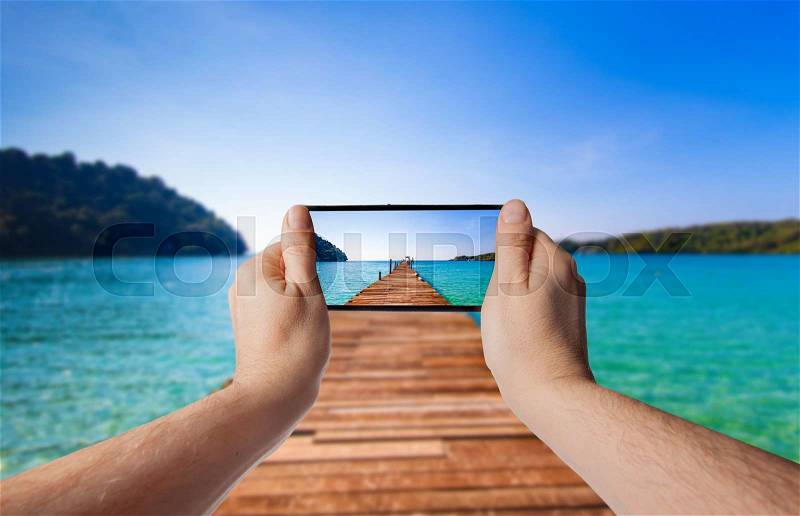 Tourism Concept. Old wooden pier. paradise island. Hand with a smartphone. Taking photo, stock photo