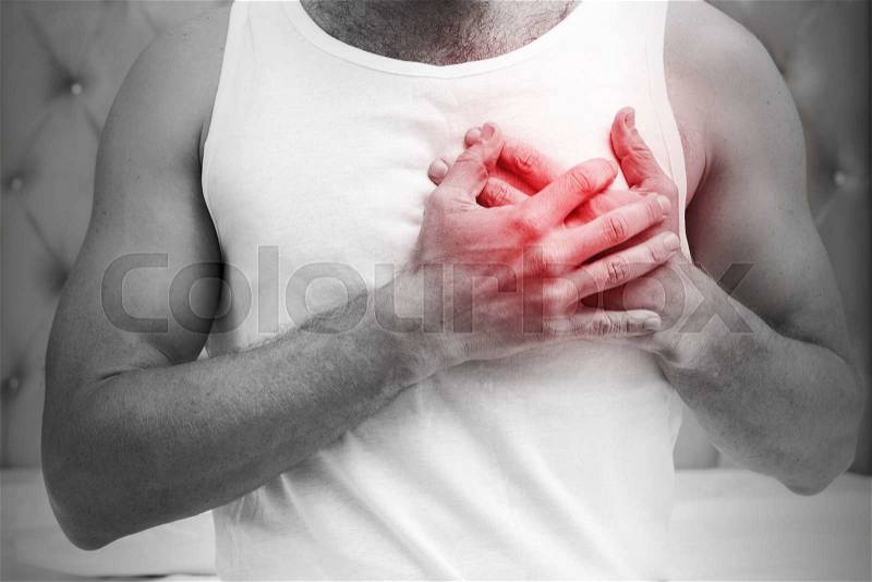 Heart pain gesture. Young sporty Caucasian man in white shirt holds hands near his heart. Black and white stylized photo with red local ache spot, stock photo