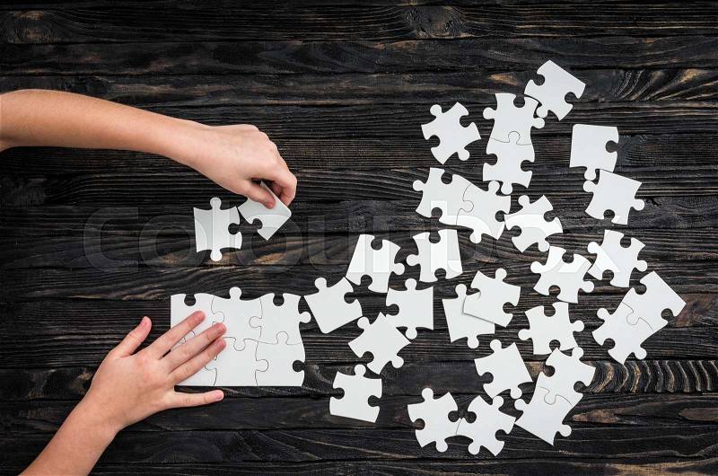 Hands starting to collect puzzle pieces on dark wooden table, stock photo