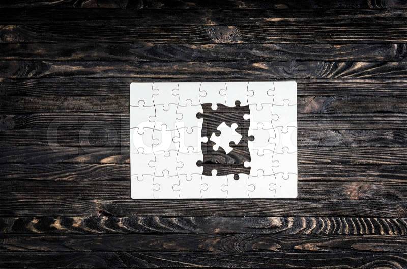 White started puzzle with uncompleted center on dark wooden background, stock photo