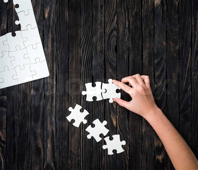 Hand starting to collect puzzle pieces on dark wooden table, stock photo