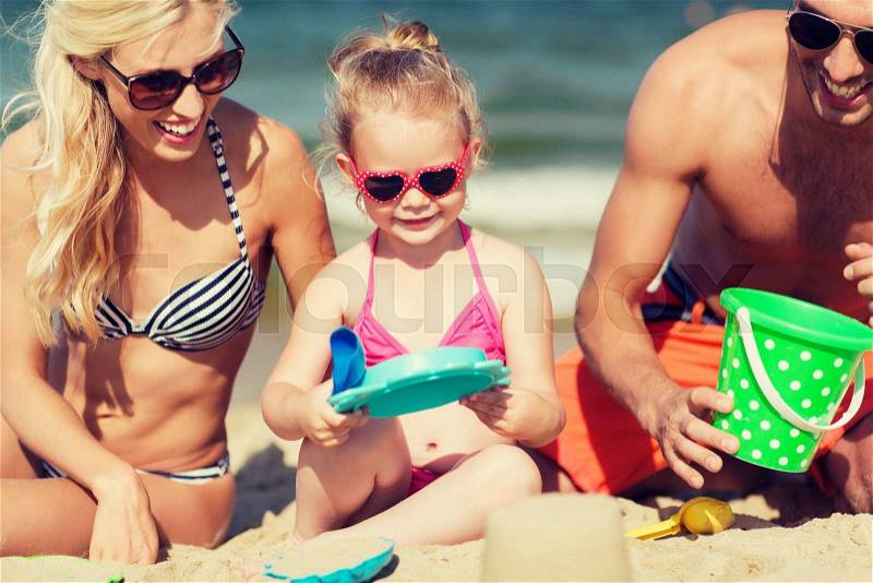 Family, travel, vacation and people concept - happy man, woman and little girl in sunglasses playing with sand toys on summer beach, stock photo