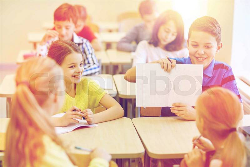 Education, elementary school, learning and people concept - group of school kids with pens writing test and showing notebook in classroom, stock photo