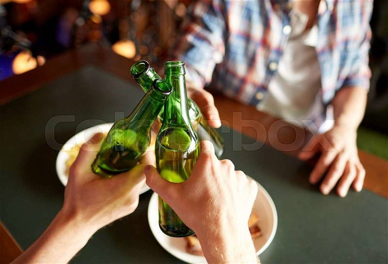 People, men, leisure, friendship and celebration concept - close up of male friends drinking beer and clinking bottles at bar or pub, stock photo