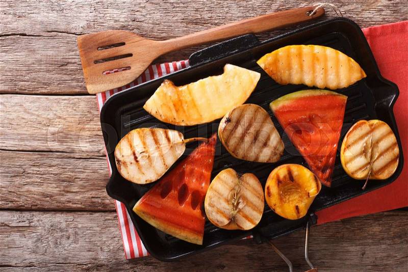 Delicious fruit apples, melon, pear, watermelon and peach on a grill pan close-up on the table. horizontal view from above , stock photo
