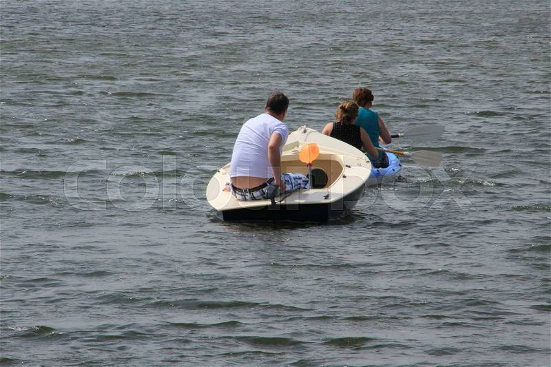 The ladies with paddles in the canoe have adverse wind and the man in the pleasure boat with motor push the canoe forwards on the lake in the park in Simonshaven in the summer, stock photo