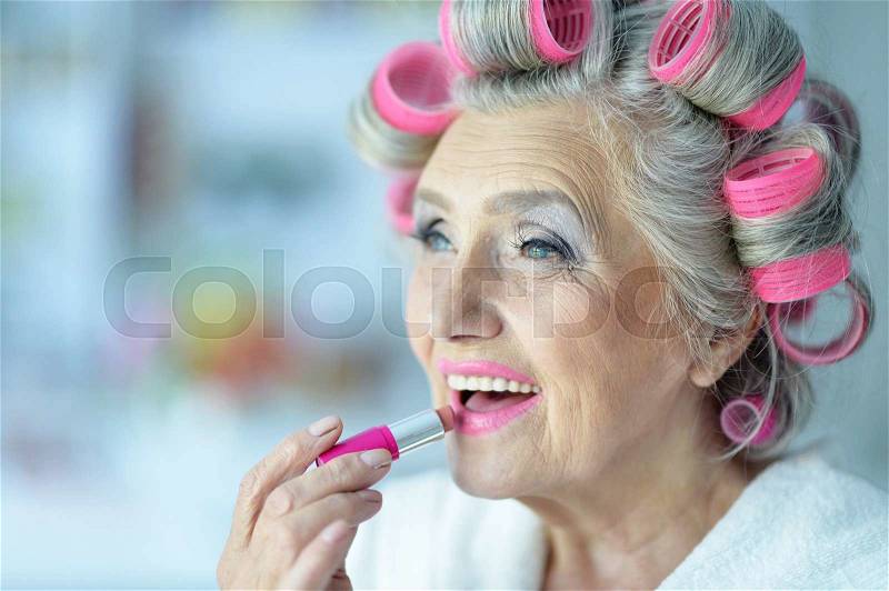 Senior woman in hair rollers with lipstick at home, stock photo