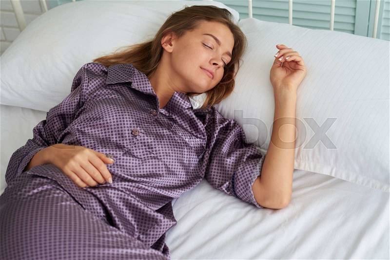 Beautiful woman in satin pajamas is sleeping peacefully on white bedding, stock photo