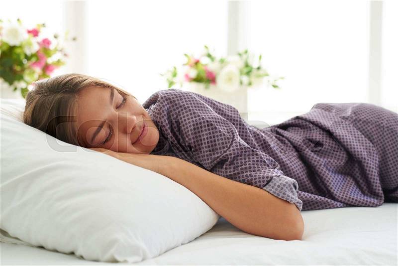 Close-up of beautiful woman in satin pajamas sleeping peacefully on white pillow in light cozy bedroom, stock photo