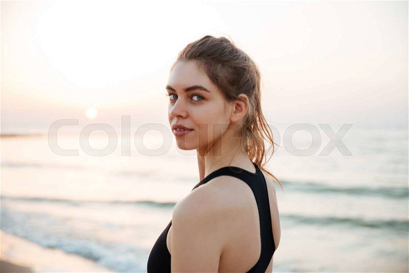 Young runner woman smiling happy resting after jogging training on beach at sunset, stock photo