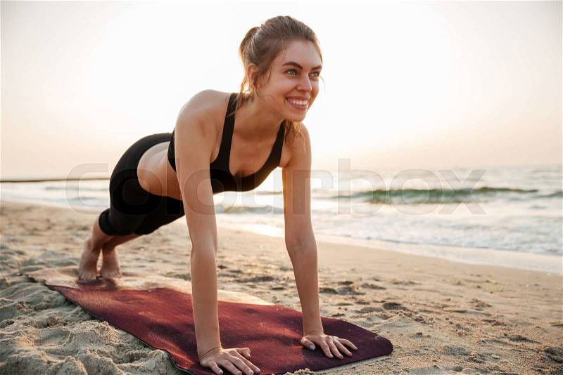 Portrait of a young woman stretching on yoga mat outdoors at the beach, stock photo